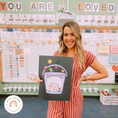 @teachinglittlemindss standing in front of her Boho Vibes classroom wall holding a teacher introduction card.