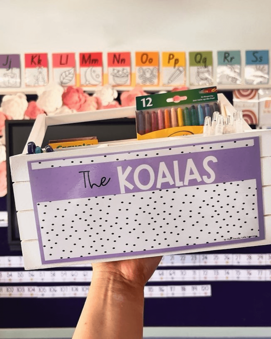 The left image shows a hand holding up a tub of art supplies. It has a label with the term ‘The Koalas.’ In the background, we see a classroom wall with colourful alphabet posters. They’re all a part of the Spotty Brights range. The right image features printout resources from the same range. We see a ‘Morning Greeting’ poster and items for an Affirmation Station.