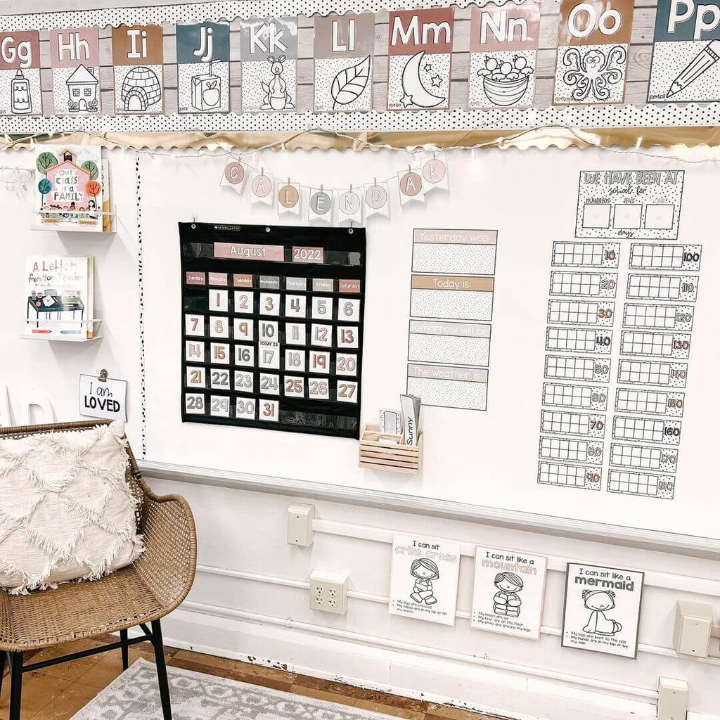 A classroom whiteboard is filled with display items from the Spotty Boho Range. We see a calendar display, a row of alphabet posters, and bunting letters that spell ‘calendar.’ The colours are muted neutrals, blues, browns and dusty pinks. There’s also a cane armchair and a light grey and white rug in the corner of the image.
