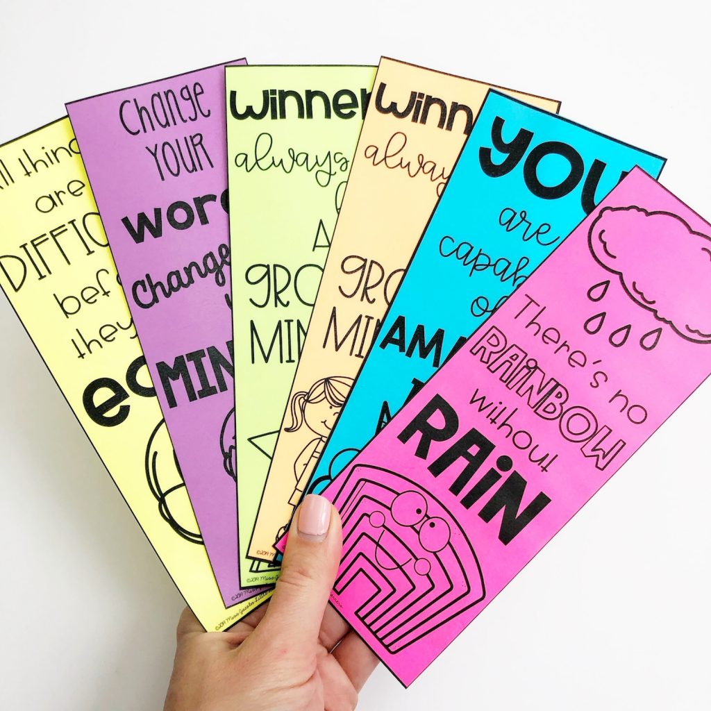A hand holds six colourful growth mindset bookmarks with affirmations printed on them.