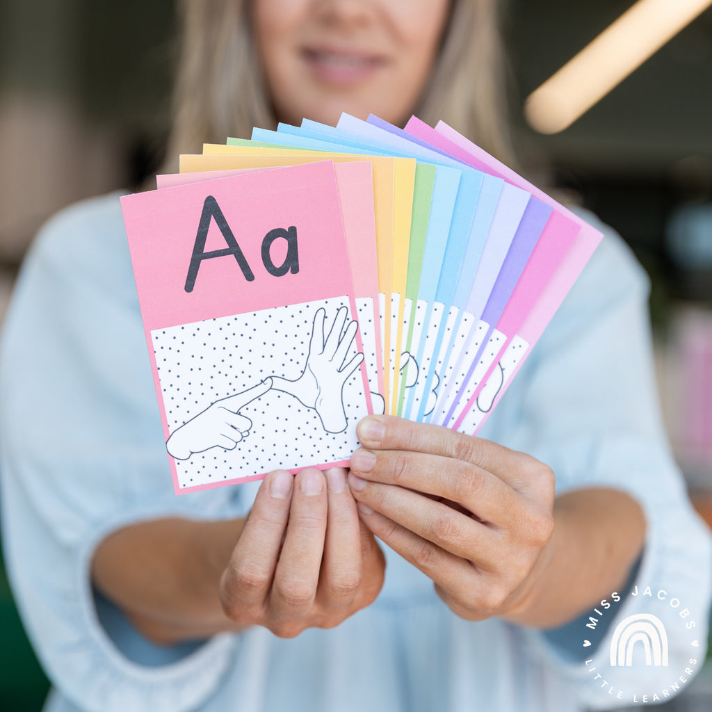 Chantelle holds a series of Auslan Alphabet posters in the Spotty Brights theme. The first card is visible and it shows an illustration of two hands fingerspelling the ‘A’ letter in Auslan, with the upper and lower case letter ‘A’ above it.