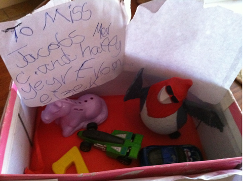 a box of nik naks with a note that reads "To miss Jacobs, Mer C and happy year, From Eizek" written in messy children's hand writing