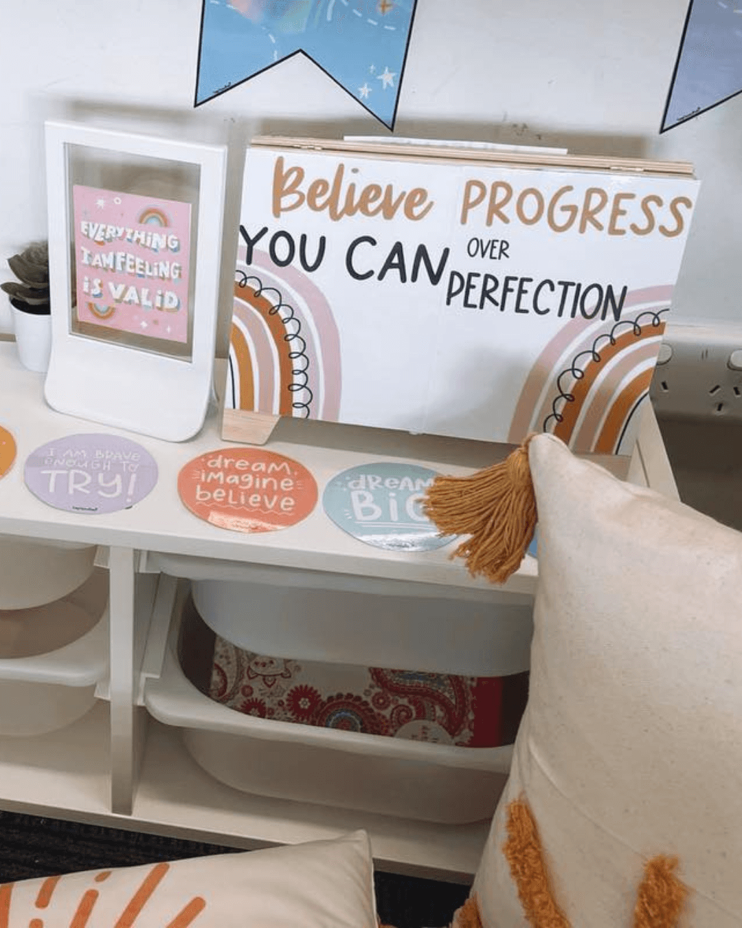 The left image shows a corner of an office with motivational posters, fairy lights and a floral wreath. The posters say things like ‘You are welcome here’ and ‘Dream Big. The right image shows a shelving unit with motivational decor and posters, including a large poster that says ‘Believe you can, Progress over Perfection.’