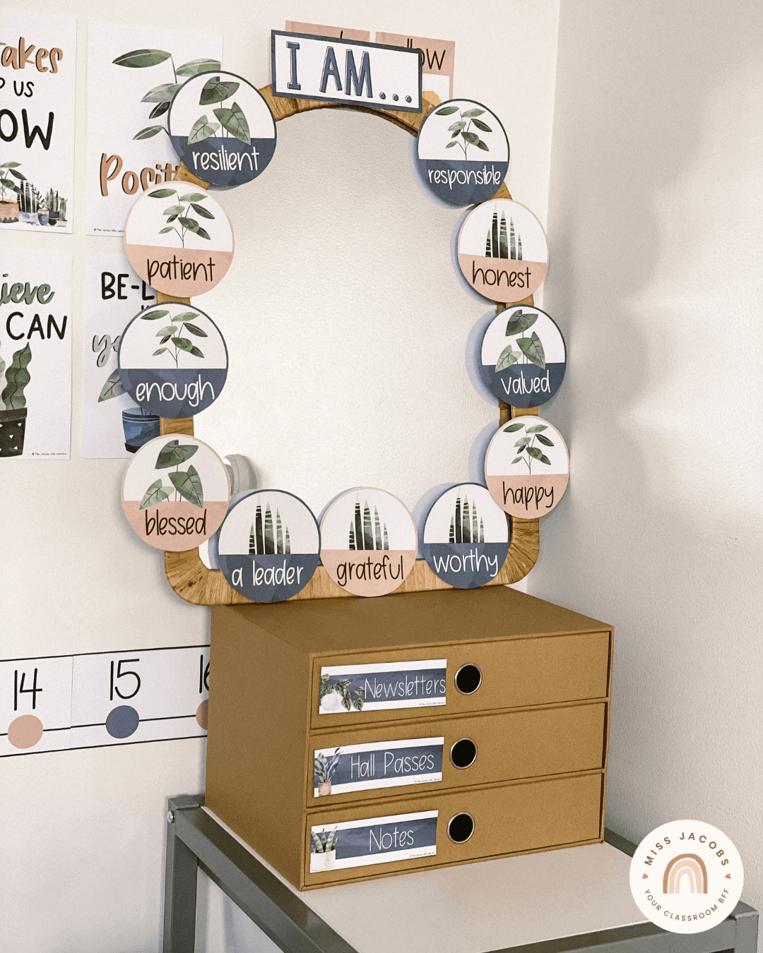 Two images show a Boho Plants Affirmation Station Display. There’s an arch-shaped mirror with round cutouts along the border that feature words like patient, blessed and grateful. The design features plant illustrations above a blush and grey coloured base.” style=