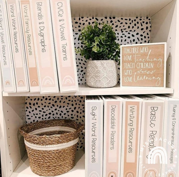 Two shelves contain a series of Boho Rainbow Folders, a basket and a pot plant. A small timber sign with white calligraphy reads ‘Teaches who love teaching, teach children who love learning.’