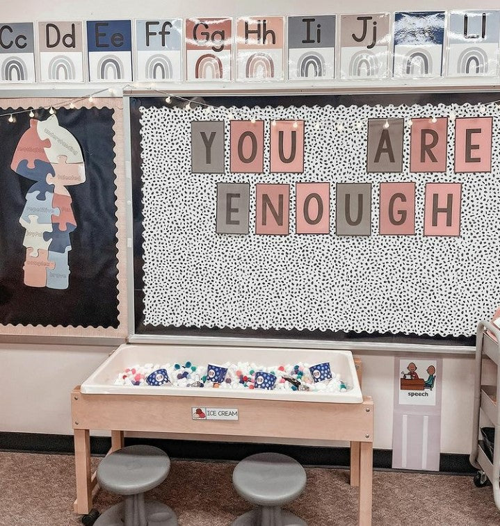 A whiteboard is covered in our Spotty background with large bulletin board letters in Boho colours that spell “You are enough.” In front of this display, a play stations is set up  for kids to make ‘ice cream’ using multi coloured cotton balls and cups.