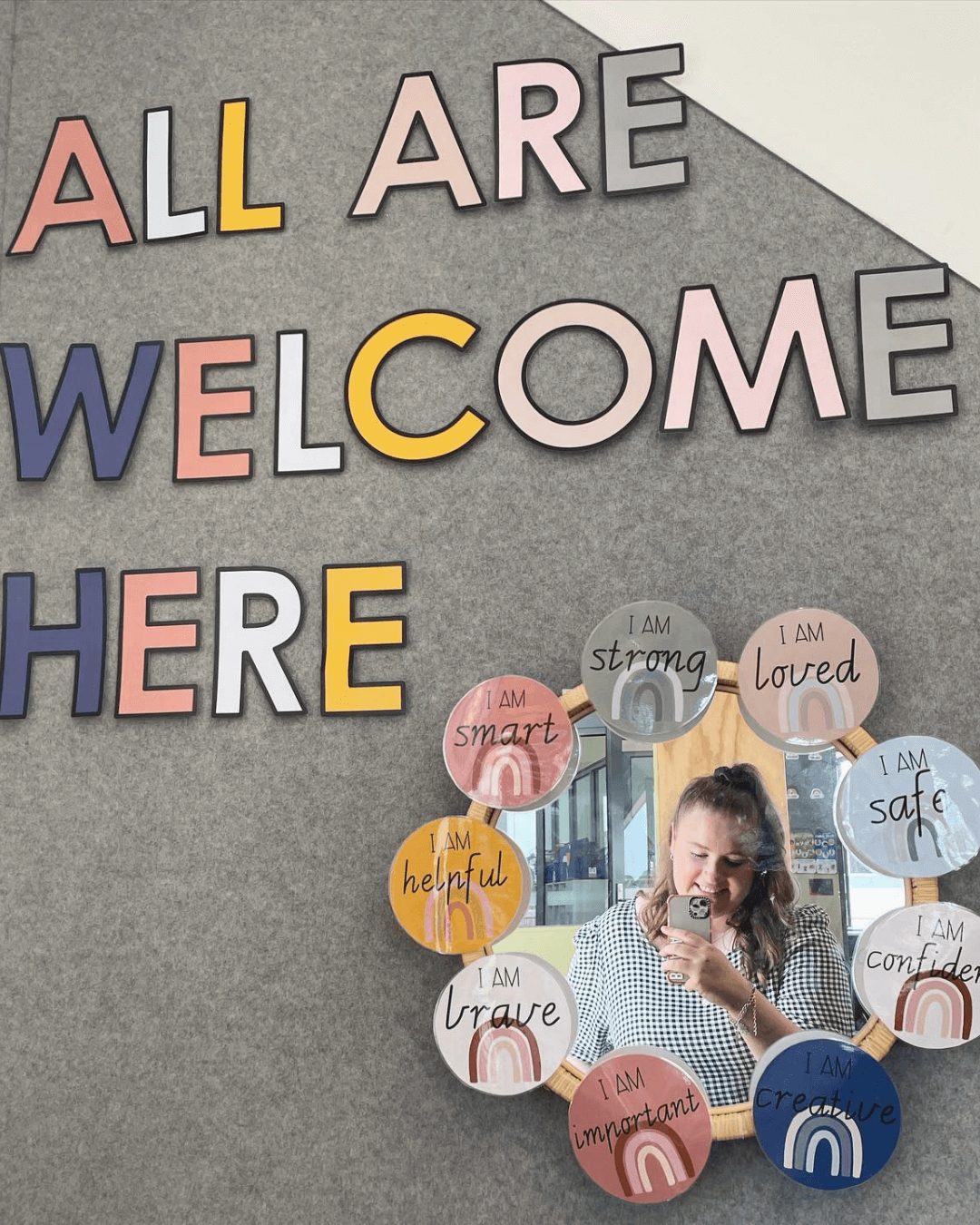 The left image shows a display that reads ‘All are welcome here.’ the right image shows a teacher standing in front a classroom. Boho Rainbow Alphabet Posters line the top of the board. Blue letters spell ‘So happy you’re here!’
