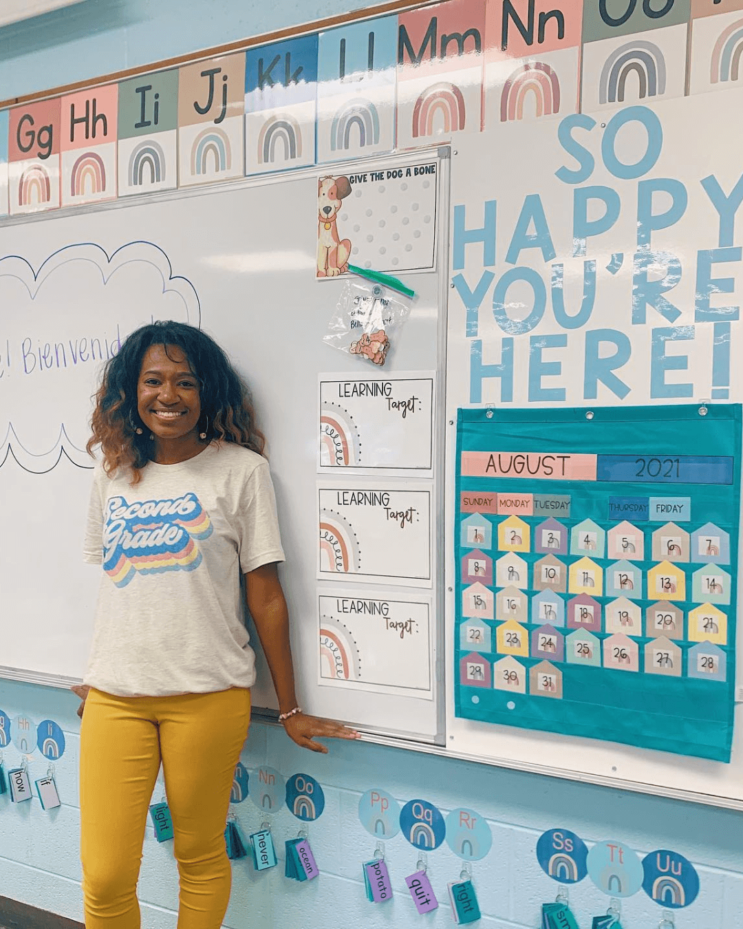 The left image shows a display that reads ‘All are welcome here.’ the right image shows a teacher standing in front a classroom. Boho Rainbow Alphabet Posters line the top of the board. Blue letters spell ‘So happy you’re here!’