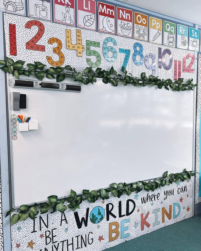 A classroom whiteboard is surrounded by colourful number and letter posters in my Spotty Brights theme. The whiteboard is bordered by leaves, with a display that reads “In a world where you can be anything, be kind” underneath.