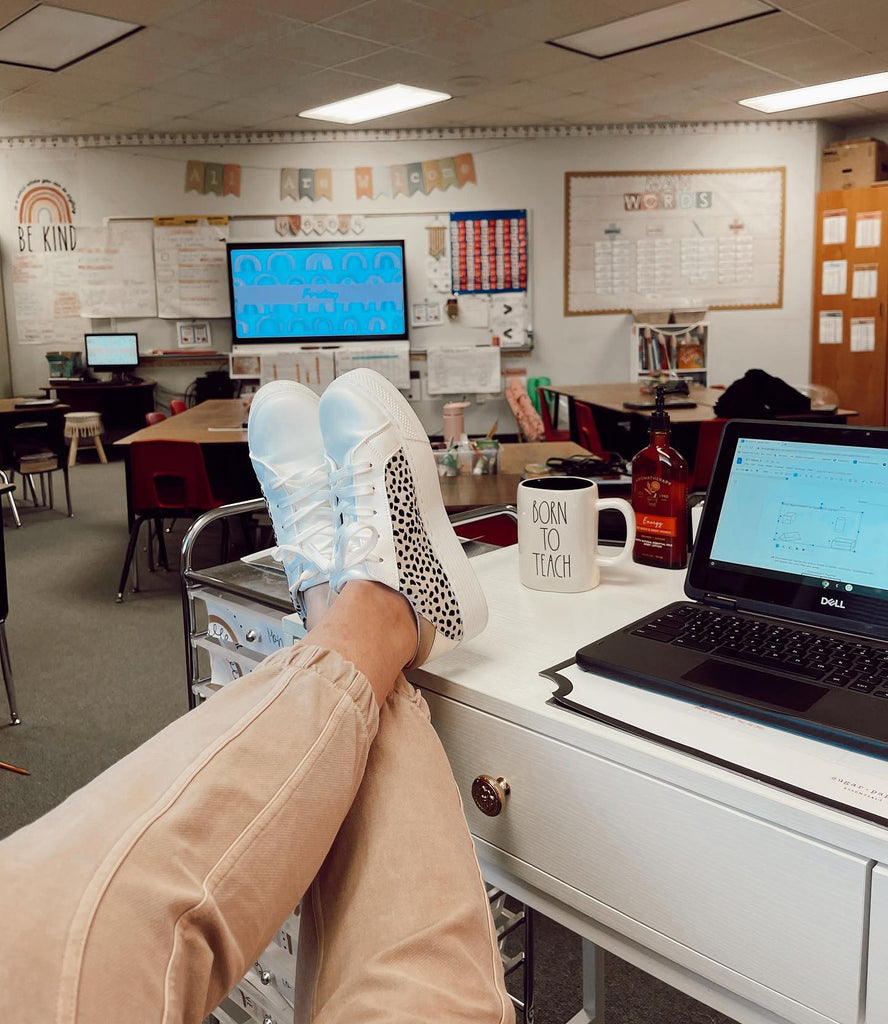 A photo is taken from a teachers’ point of view with her feet on her desk, and a classroom in the background. Her mug says ‘Born to teach.’