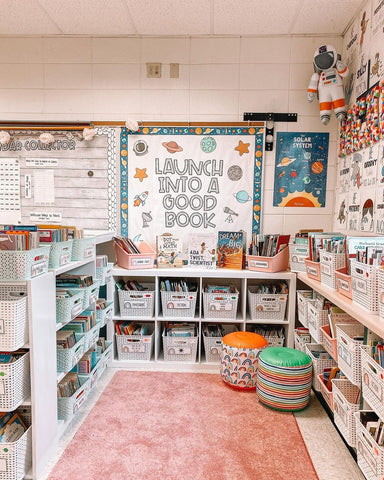 A beautiful space-themed classroom library has been set up in the corner of Lauren’s classroom. The bottom half of the wall is taken up with shelves filled with book baskets, and on the wall above the shelf is a bulletin board that reads “Launch into a good book.”