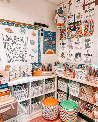 A beautiful space-themed classroom library has been set up in the corner of Lauren’s classroom. The bottom half of the wall is taken up with shelves filled with book baskets, and on the wall above the shelf is a bulletin board that reads “Launch into a good book.”