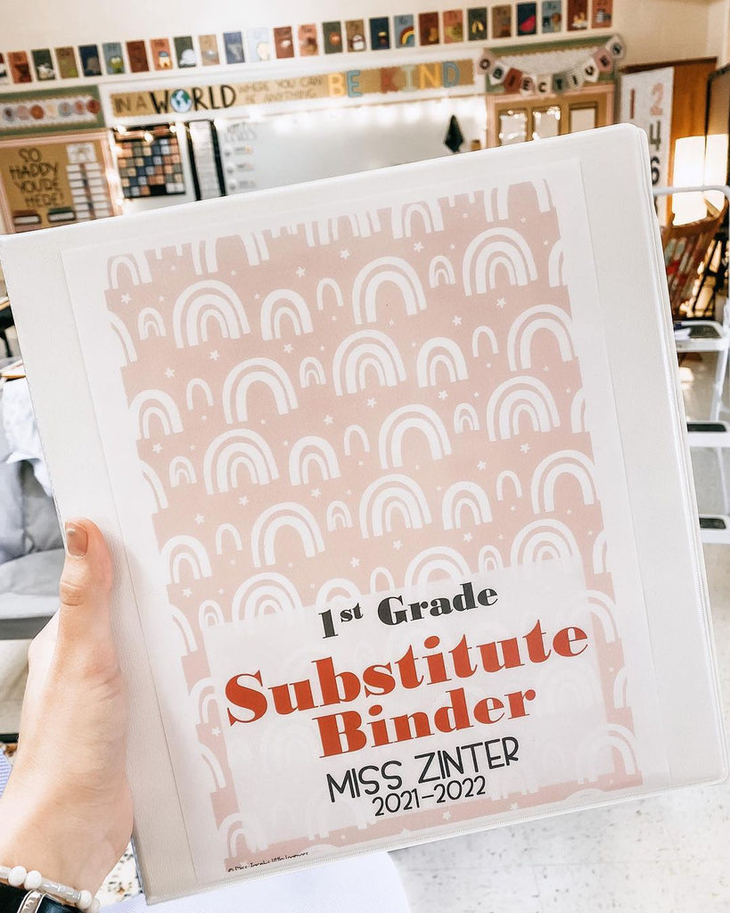 A hand holds up a white folder that reads “Substitute Binder” and has a pink cover decorated with rainbows.