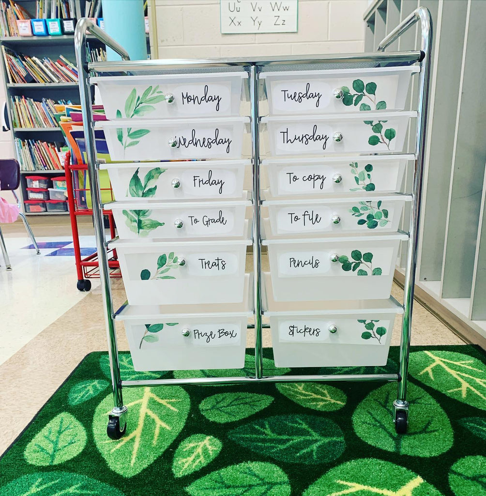 Two images show different applications of the Botanics Collection. On the left a trolley sits on top of a green rug with a leaf pattern. The draws are labelled with the words treats, pencils, stickers, prize box as well as the days of the week. On the right, a small teacher toolbox is labelled with small botanical labels and contains items like safety pins, thumb tacks, stickers and whiteout.