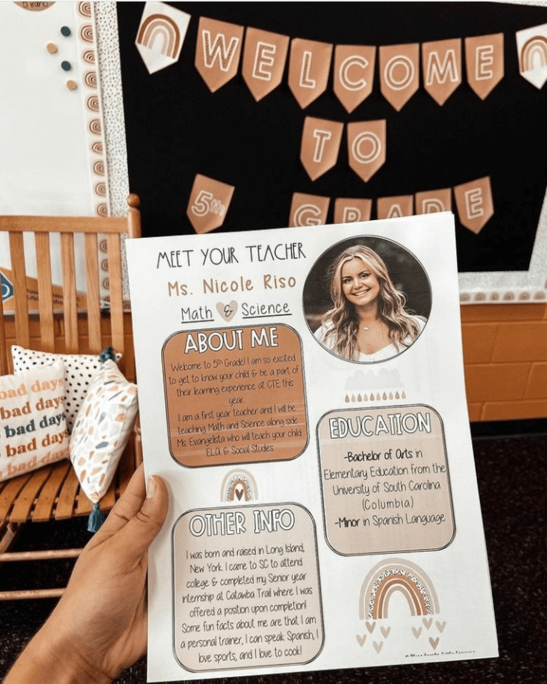 Two teachers hold up their ‘Meet your Teacher’ templates. We only see their arm, and in the background we see beautiful neutral hued classrooms.