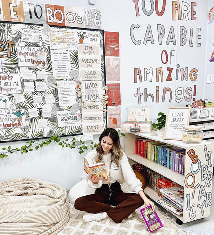 Miss Gosse reading on a bean bag in her boe ho/ nature decor classroom