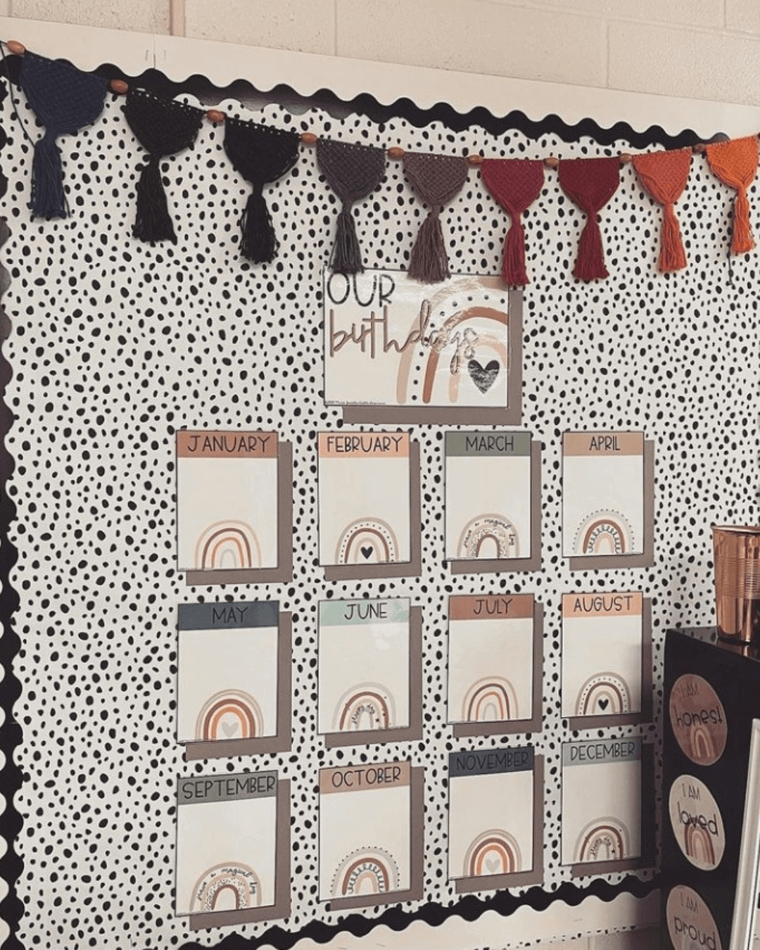 The left image shows a boho themed birthday display with black and white spotted wallpaper and fringed bunting in deep autumnal colours. The right image has three small stools and a long bench and the same spotted wallpaper in the shape of a house on the wall.” style=