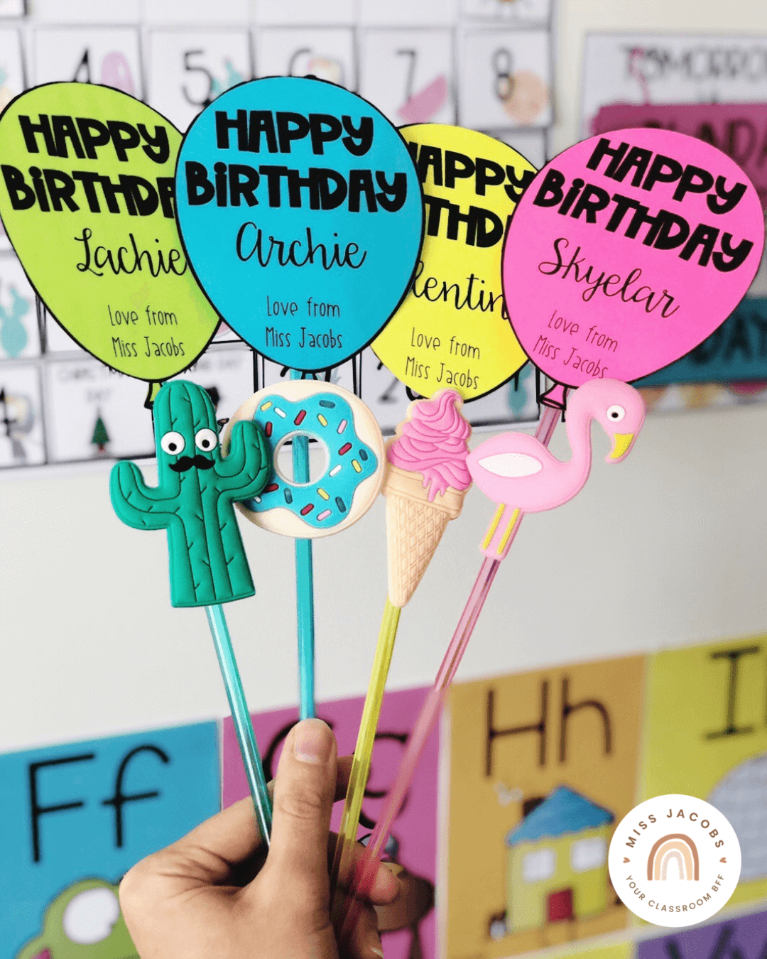 The left image shows a hand holding four straws with toppers in bright colours - we see a cactus, donut, icecream and flamingo. There’s coloured balloons that say ‘Happy Birthday’ as well as the students’ name and ‘Love from Miss Jacobs.’ The right image has the same balloon labels, but they’re affixed to bright flower shaped highlighters.” style=