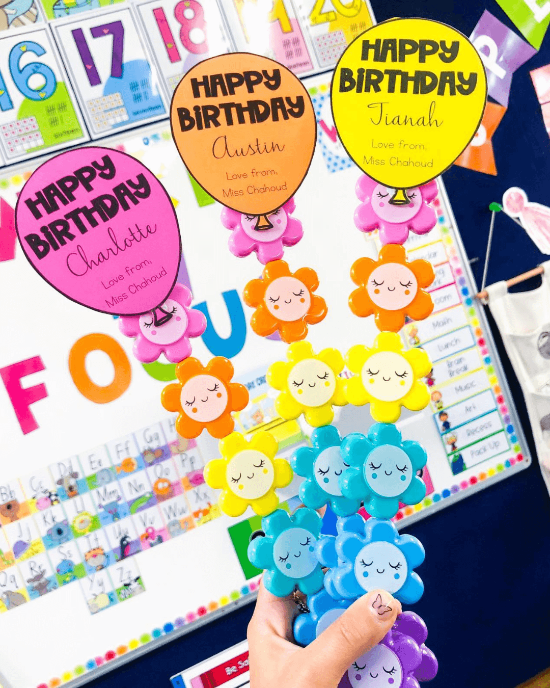 The left image shows a hand holding four straws with toppers in bright colours - we see a cactus, donut, icecream and flamingo. There’s coloured balloons that say ‘Happy Birthday’ as well as the students’ name and ‘Love from Miss Jacobs.’ The right image has the same balloon labels, but they’re affixed to bright flower shaped highlighters.