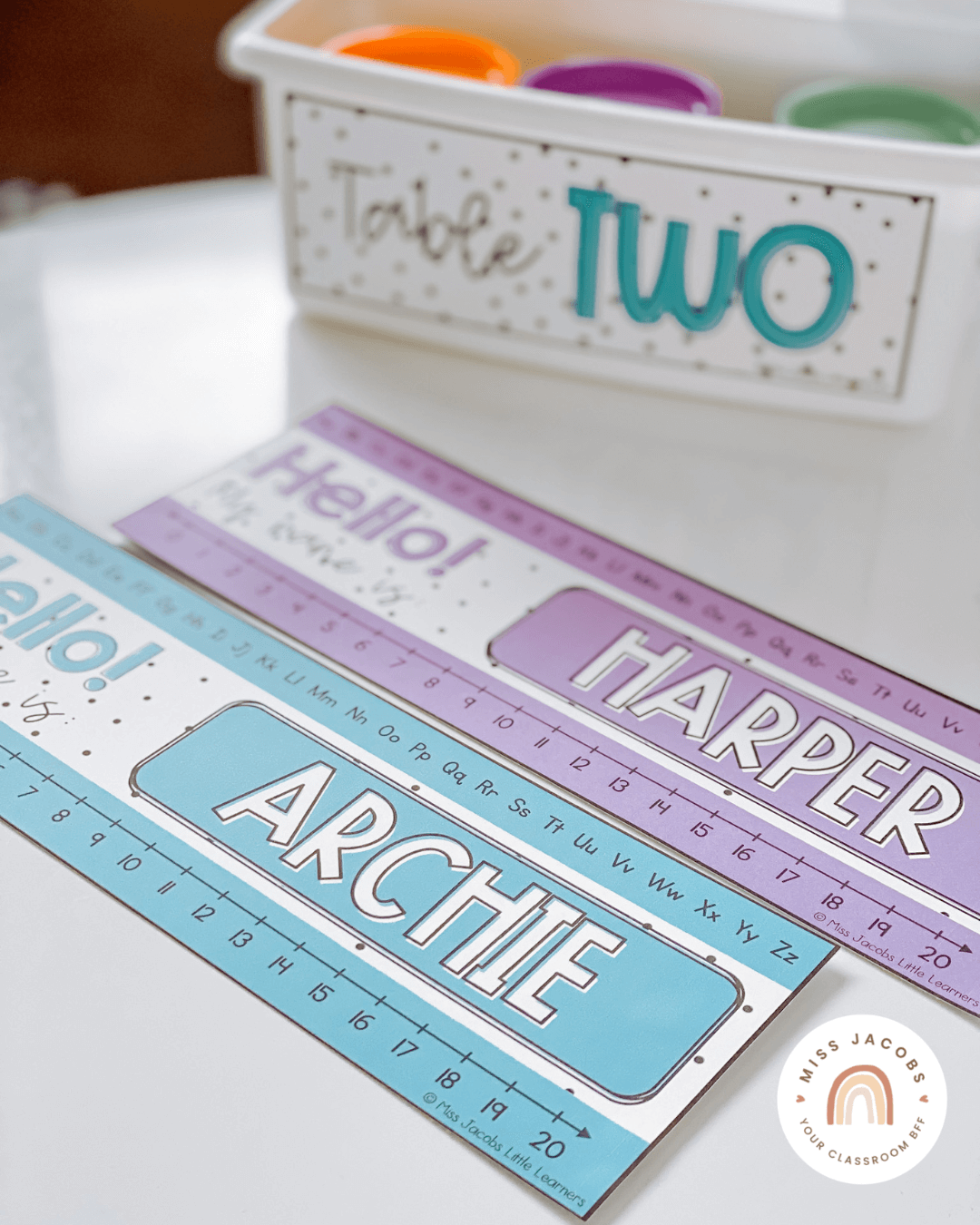 Two images show bright name tags on a desk, and on a series of white tubs on a trolley. The labels are in purple, blue and green with a spotted background.” style=