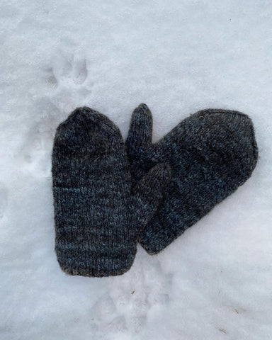 A photo of a pair of blue & black marled knit mittens in the snow near dog paw prints