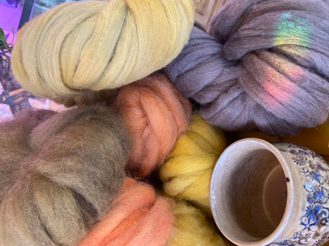 Bundles of naturally dyed wool sit next to a cup of coffee with a rainbow from the window across it