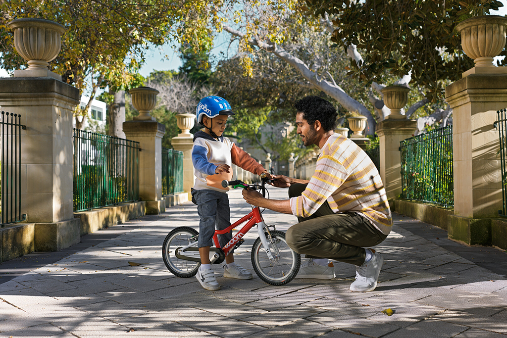 Kleiner junge stellt mit Hilfe des Vaters sein rotes Woom Kinderfahrrad ein