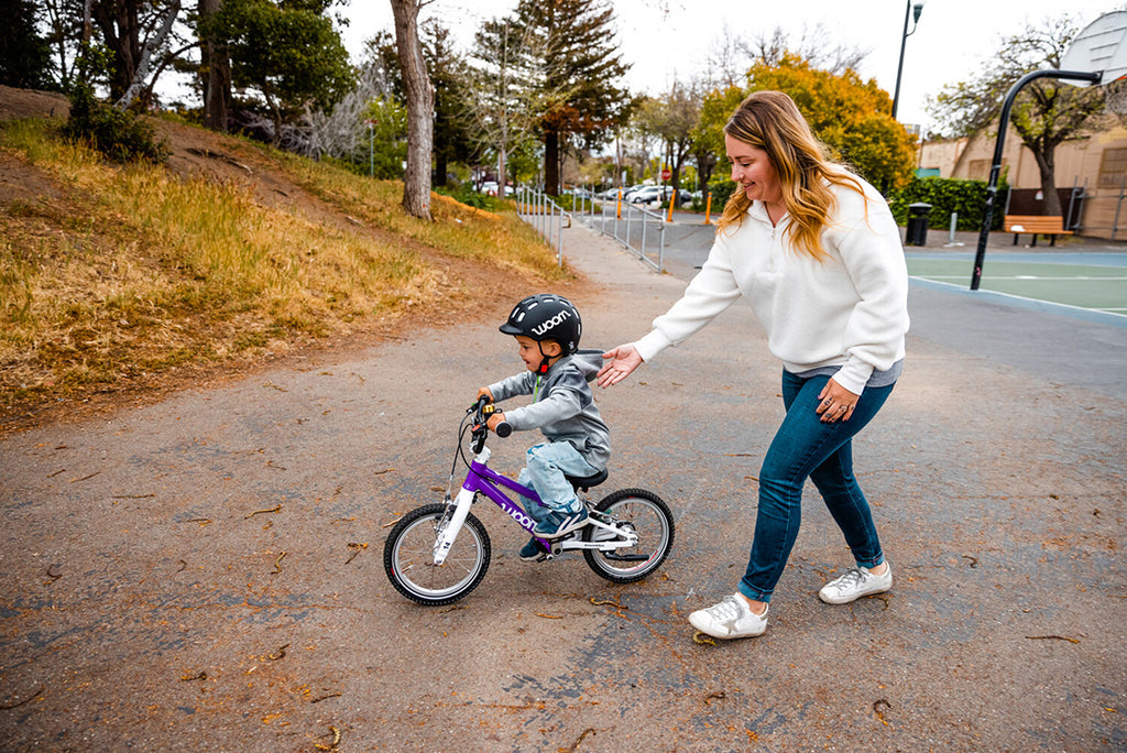 Mutter hilft ihrem Kind beim fahren eines Lianen Woom Laufrads