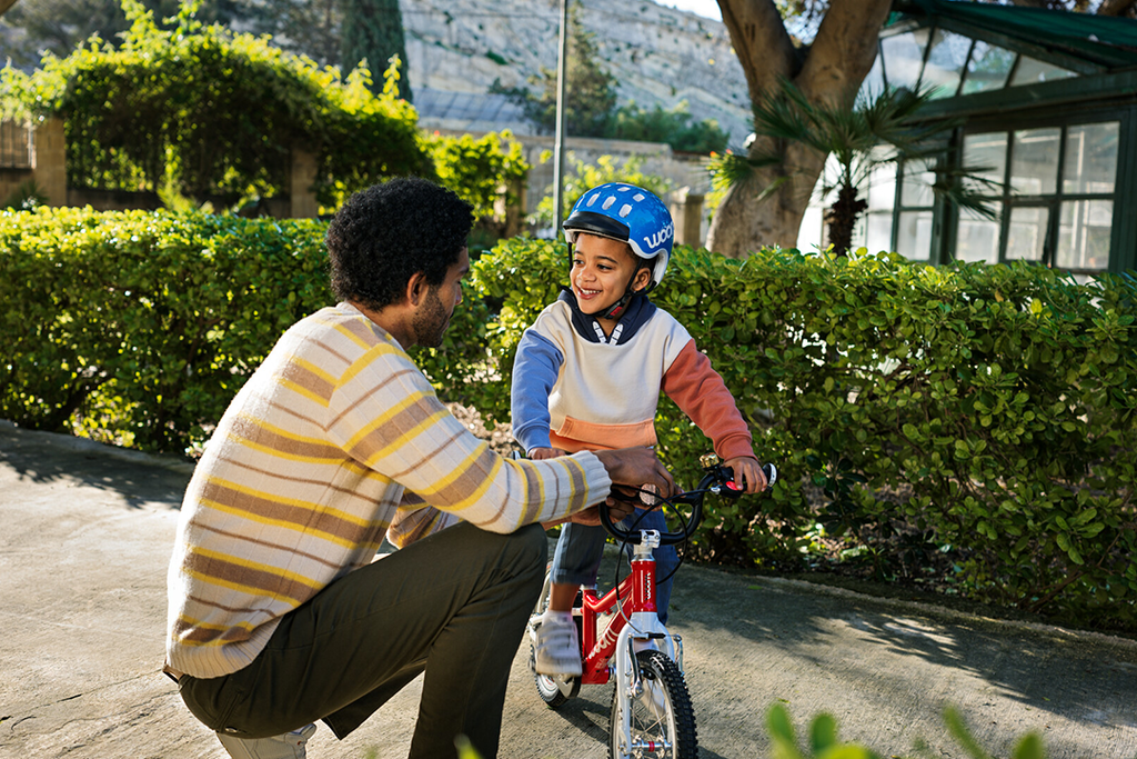 Mann bringt kleinem Kind das Fahrradfahren auf einem Woom Kinderfahrrad bei