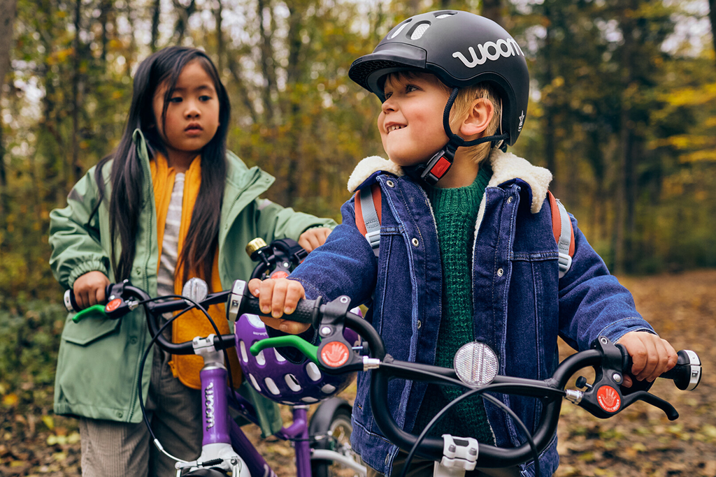 Zwei Kinder stehen mit ihren Woom Kinderfahrrädern im herbstlichen Wald
