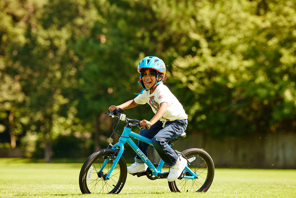 Junge mit Fahrradhelm fährt mich herausgestreckter Zunge auf blauem Forme Kinderfahrrad