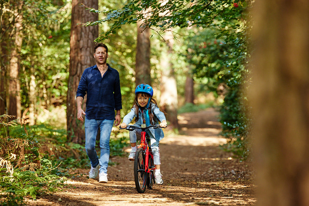 Kind fährt auf ihrem roten Forme Kinderfahrrad neben ihrem Vater auf einem Waldpfad