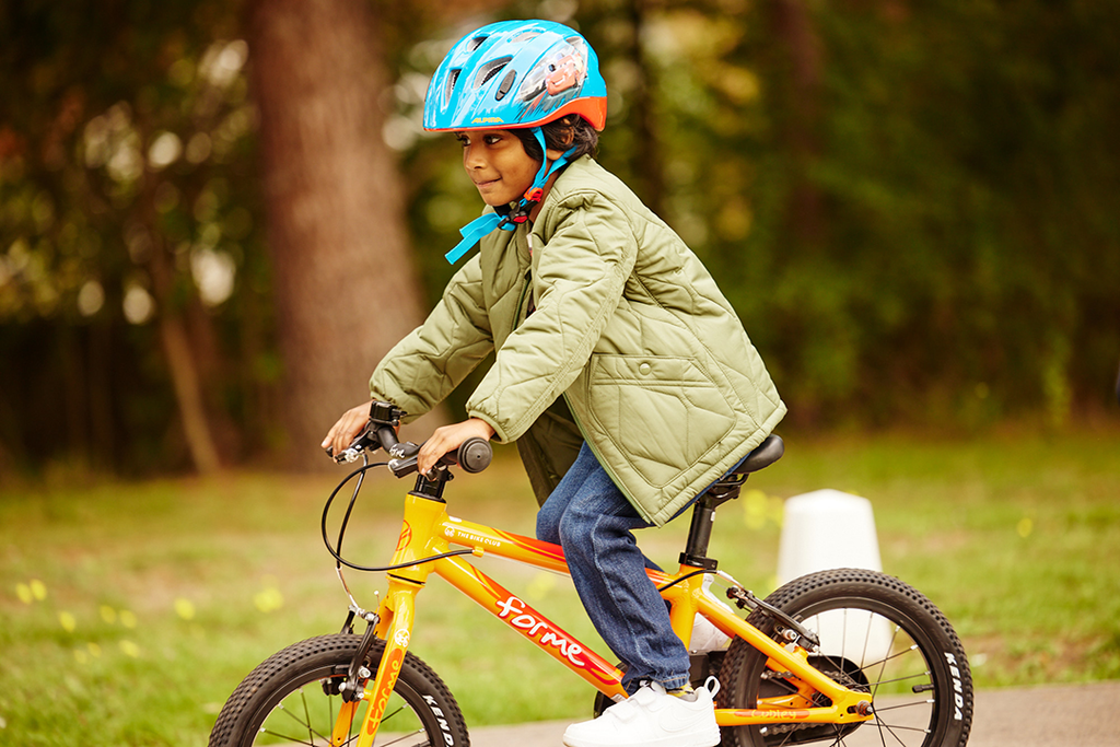 Junge mit Fahrradhelm fährt auf orangefarbenem Forme Kinderfahrrad