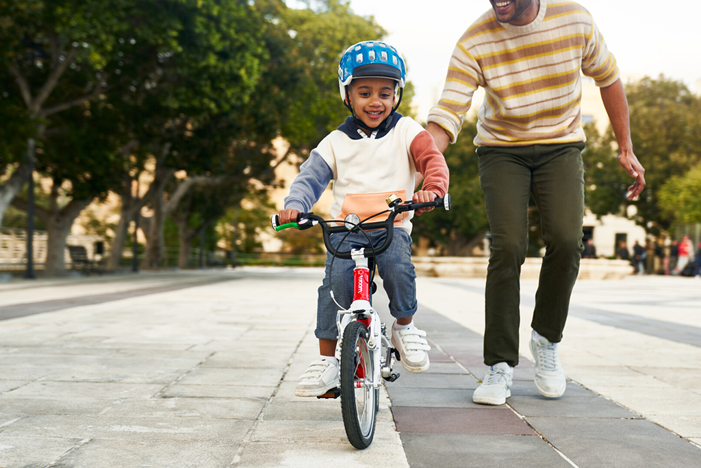 Mann hilft Kind beim Fahrradfahren lernen mit Woom Kinderfahrrad
