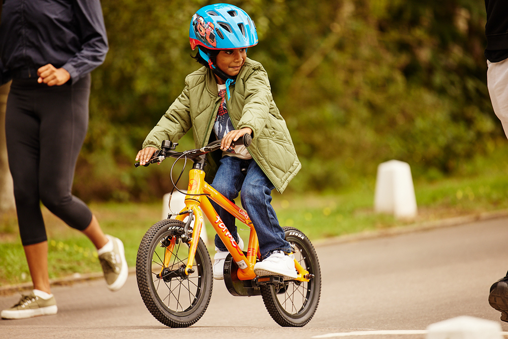 Junge mit Fahrradhelm fährt auf orangenem Forme Kinderfahrrad