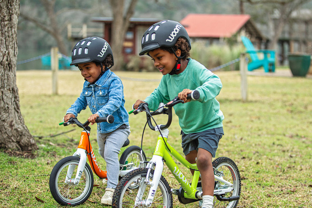 Zwei Kinder fahren auf Woom Kinderfahrrädern auf einer Wiese