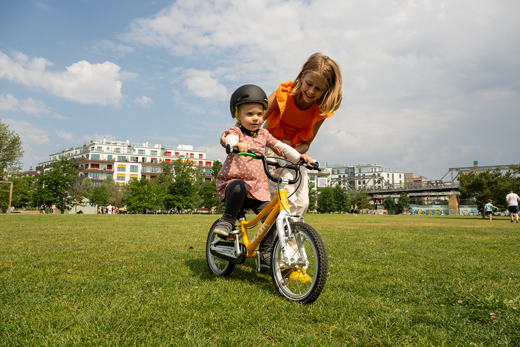 Mädchen hilft Kleinkind beim Fahrradfahren auf einer Wiese
