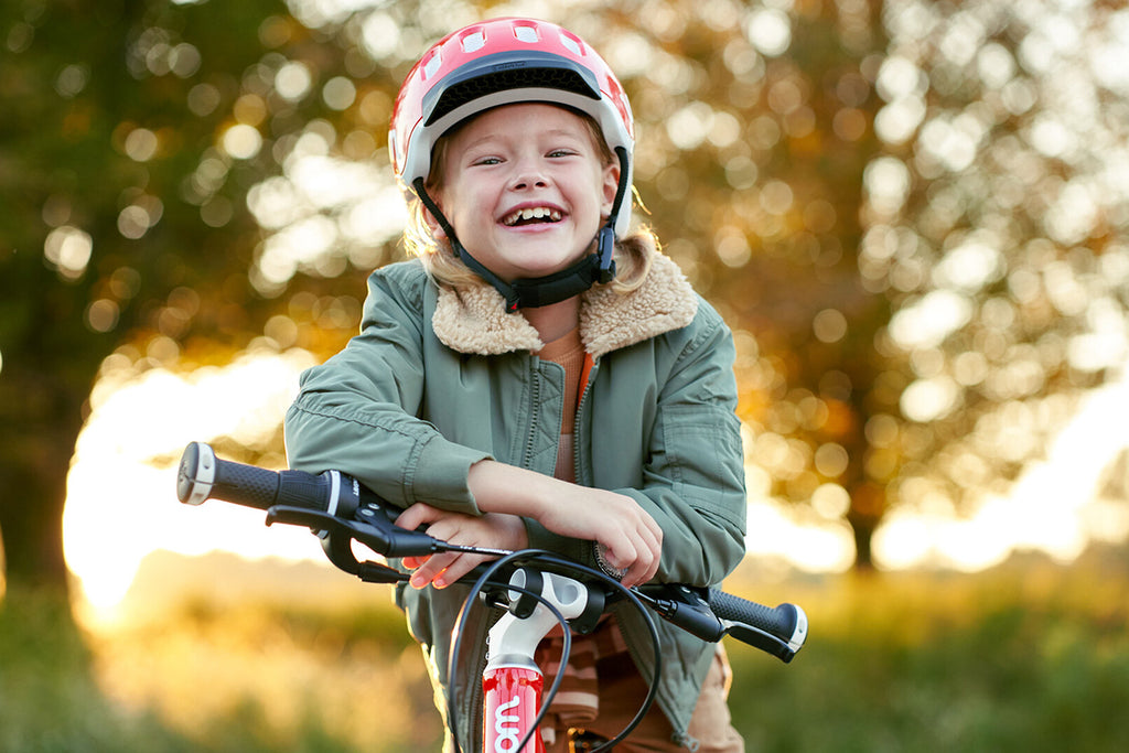 Mädchen mit Fahrradhelm lächelt und lehnt auf dem Lenker ihres Kinderfahrrads
