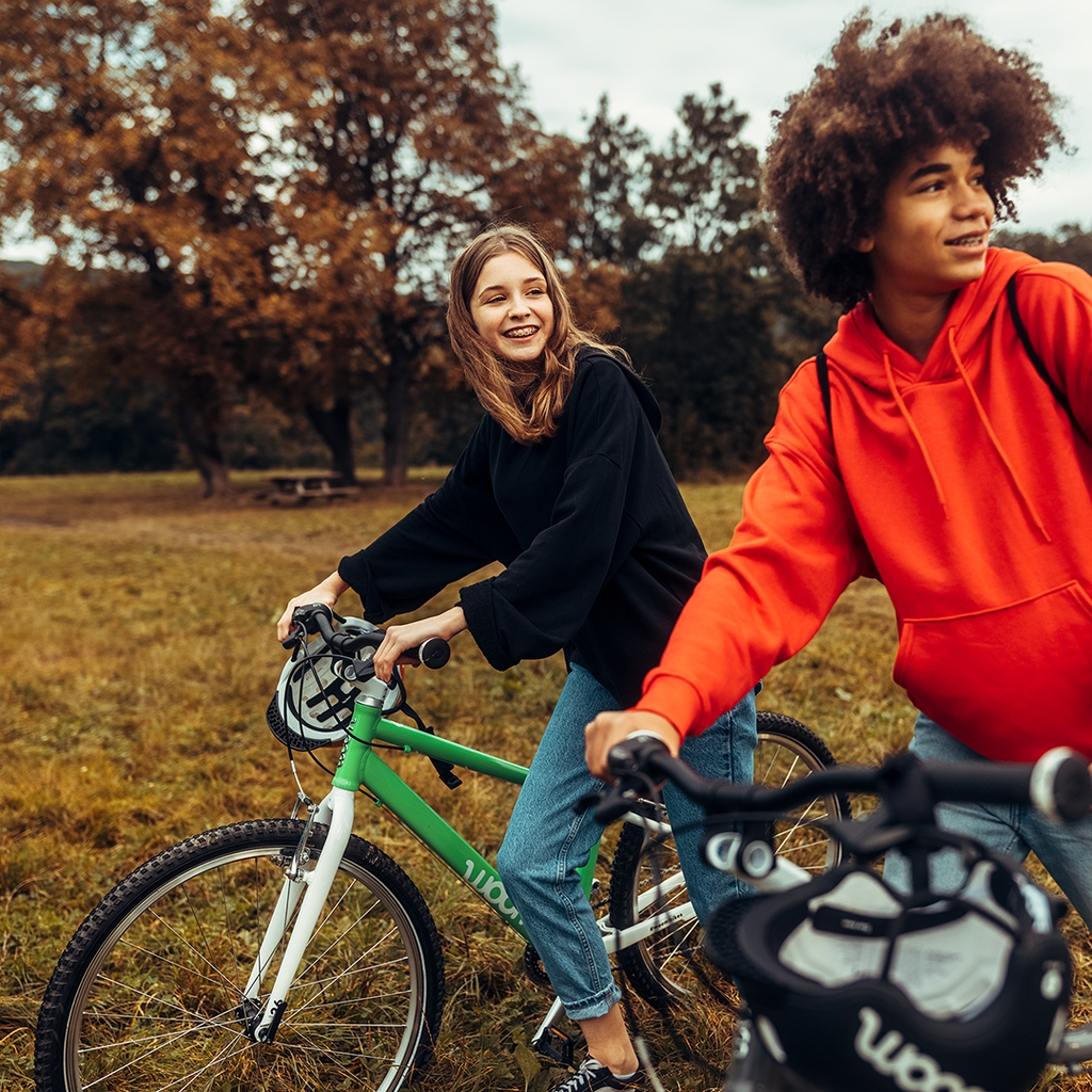 Zwei Teenager fahren auf Woom Kinderfahrrädern durch den Park