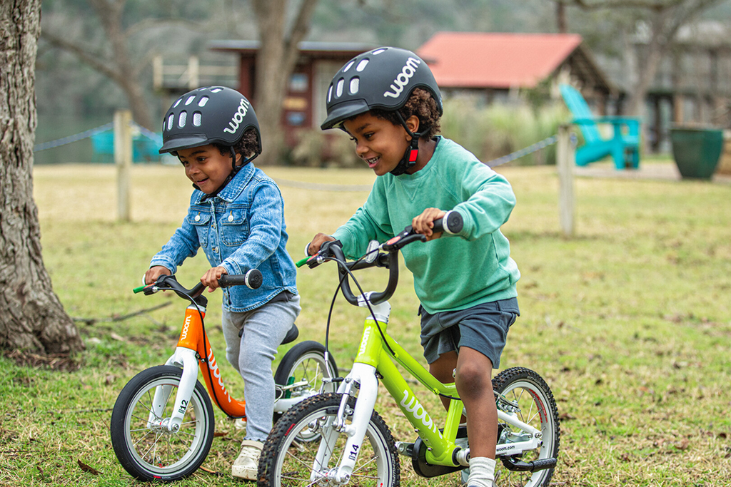 Zwei kleine Jungs fahren auf Woom Laufrädern im Park