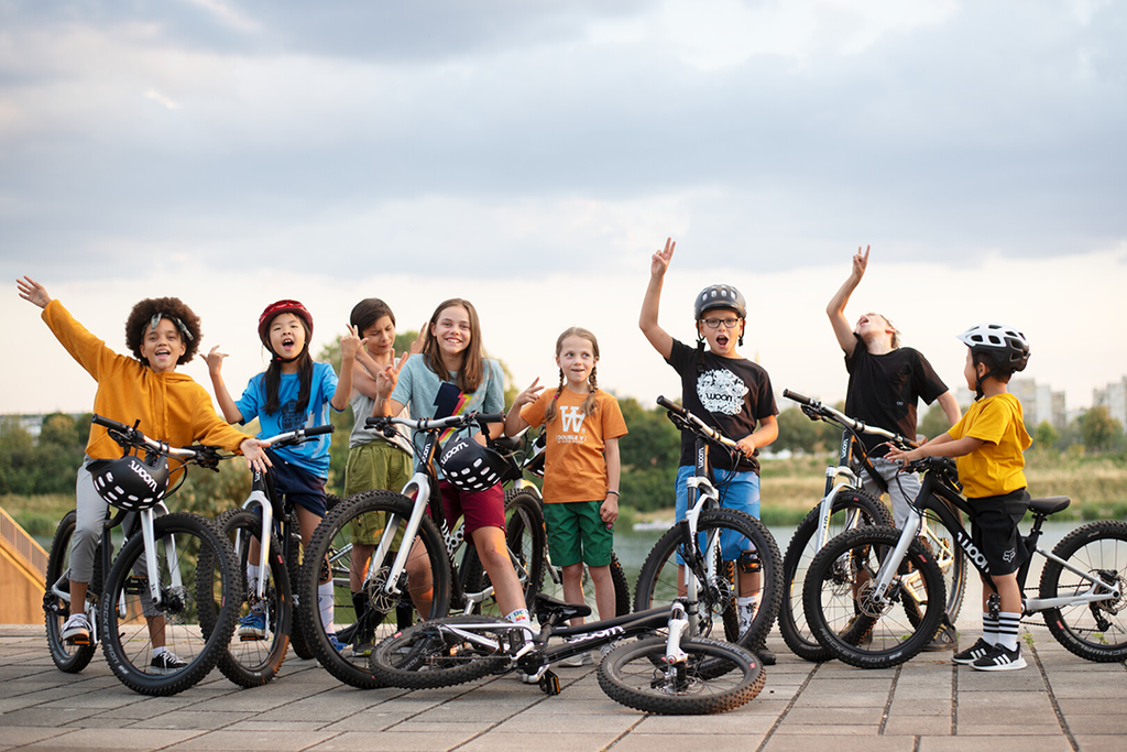 Eine Gruppe Kinder steht mit ihren Woom Kinderfahrrädern auf einem Steinboden