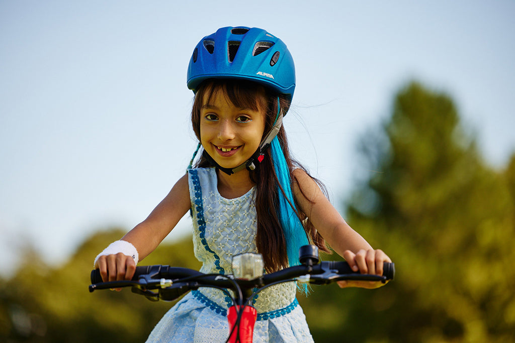 Junges Mädchen mit blauem Fahrradhelm fährt auf ihrem roten Kinderfahrrad auf die Kamera zu