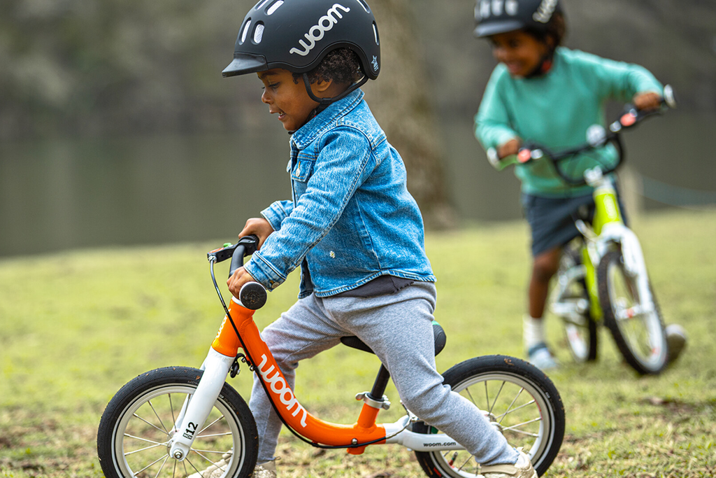 Zwei kleine Jungs fahren mit ihren Woom Laufrädern durch den Park
