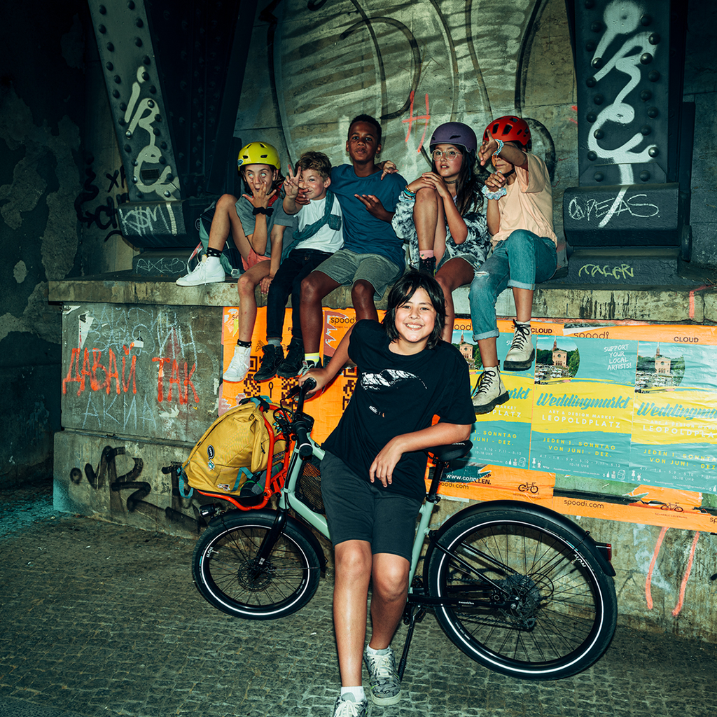 Gruppe von Teenagern vor urbanem Hintergrund mit Woom Now Kinderfahrrad