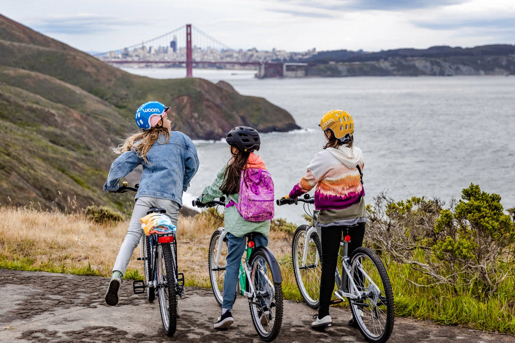 3 Kinder stehen mit Woom Kinderfahrrädern an der Küste