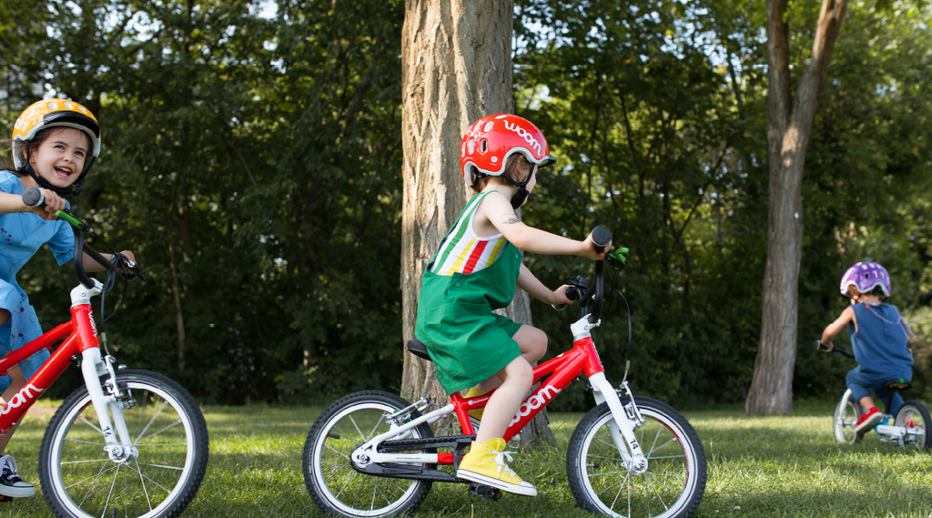 Kleine Kinder fahren mit Woom Kinderfahrrädern um einen Baum