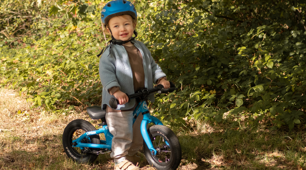 Kleiner Junge steht mit seinem blauen Forme Litton Laufrad auf einem Waldweg