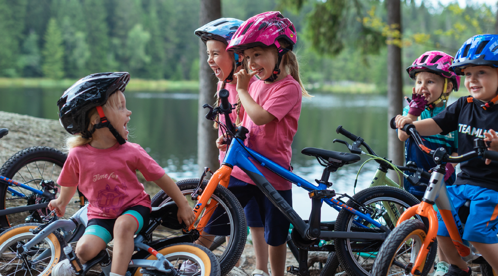 Mehrere Kinder stehen mit ihren Cube Kinderfahrrädern vor einem Waldsee