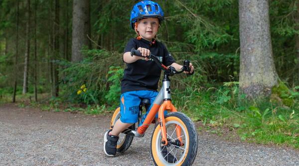 Ein kleiner Junge fährt auf einem leichten orangenen Laufrad Cube Cubie 120 Walk im Wald