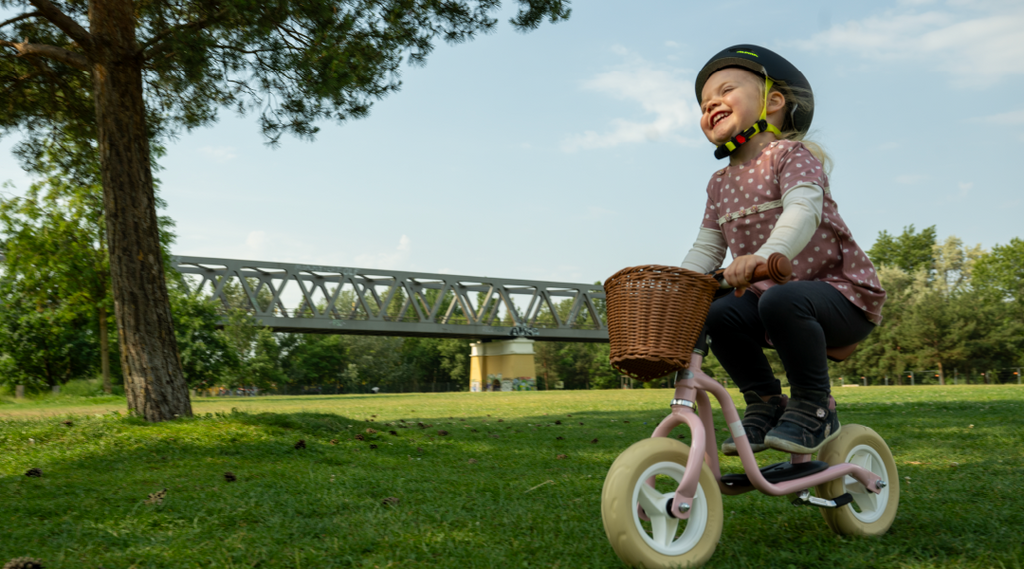 Ein kleines lachendes Mädchen radelt auf einem leichten rosa Laufrad PUKY LR M Classic im Park